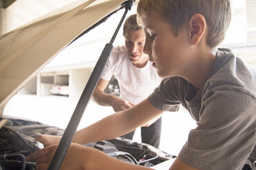Boy learning car maintenance with father under car hood - ISF08406