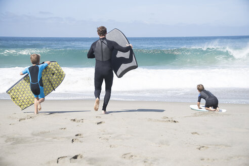 Rückansicht eines Vaters und zweier Söhne, die mit Bodyboards am Strand laufen, Laguna Beach, Kalifornien, USA - ISF08410