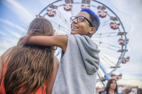 Rückansicht eines jugendlichen Paares, das vor einem Riesenrad in einem Vergnügungspark über die Schulter schaut - ISF08422