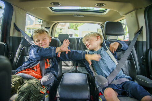Zwillingsbrüder sitzen auf dem Rücksitz eines Fahrzeugs und streiten - ISF08428