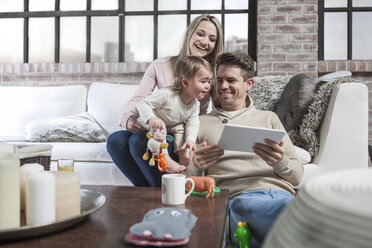 Mutter und Kleinkind sitzen auf dem Sofa, das Kleinkind schaut auf das digitale Tablet des Vaters - ISF08537