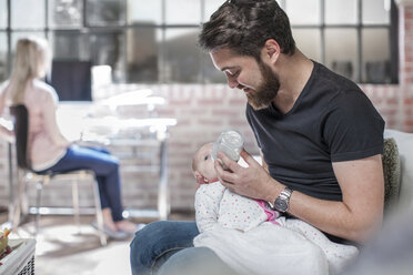 Vater sitzend, füttert kleine Tochter, Mutter am Schreibtisch sitzend, arbeitend, hinten - ISF08539