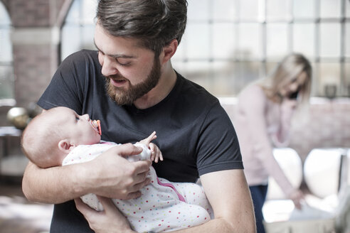 Vater hält seine kleine Tochter, während die Mutter im Hintergrund telefoniert - ISF08541