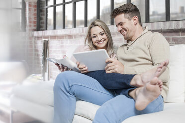 Paar zu Hause, entspannt auf dem Sofa, schaut auf ein digitales Tablet - ISF08545