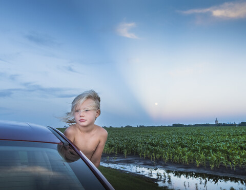 Junge lehnt sich aus dem Autofenster und schaut weg, lizenzfreies Stockfoto