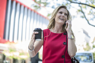 Businesswoman with takeaway coffee talking on cellphone in city - ISF08582