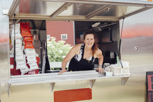 Portrait of woman leaning forward at hatch of food stall trailer - ISF08681