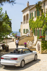Gepäckträger, der ein Paar begrüßt, das ein Cabrio zu einem Boutique-Hotel fährt, Mallorca, Spanien - CUF22654