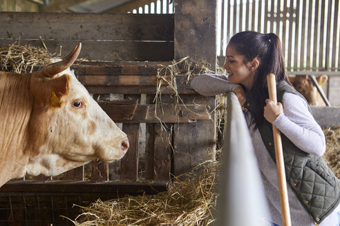 Side view of woman in barn face to face with cow - CUF22735