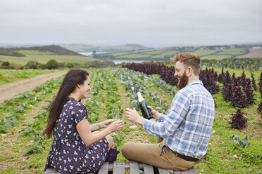 Couple in rural location sitting on pallets pouring champagne - CUF22741