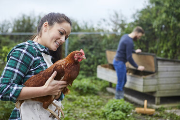 Young couple in chicken coop holding chicken - CUF22777