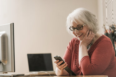 Lächelnde Frau, die ein Mobiltelefon am Schreibtisch benutzt - CUF22810