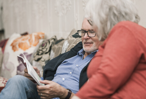 Älteres Paar liest Buch auf Couch, lizenzfreies Stockfoto