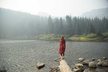 Frau in Schottenkaro-Decke eingewickelt mit Blick auf einen nebligen See, Mount Hood National Forest, Oregon, USA - ISF08752