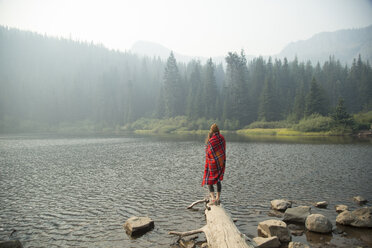 Woman wrapped in tartan blanket looking out over misty lake, Mount Hood National Forest, Oregon, USA - ISF08752