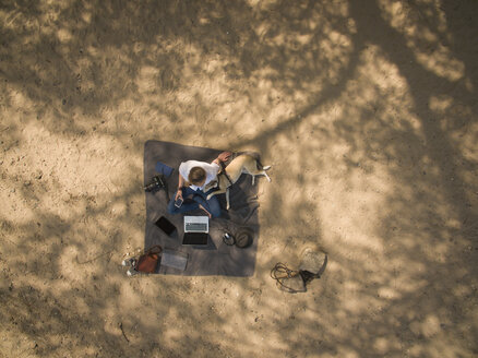 Bird's eye view of woman sitting on blanket with dog and laptop - ONF01116