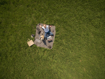 Bird's eye view of woman sitting on blanket on meadow with dog and laptop - ONF01120