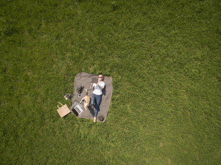 Bird's eye view of woman lying on blanket on meadow with dog using tablet - ONF01123