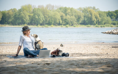 Frau auf Decke sitzend an einem Fluss mit Hund und Laptop - ONF01130