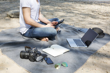 Man sitting on blanket at a beach using tablet - ONF01154