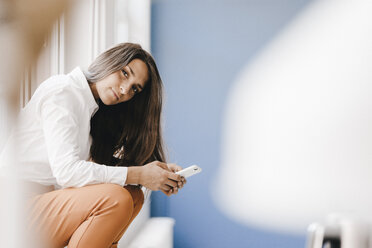 Young businesswoman sitting at window, using smartphone - KNSF03910