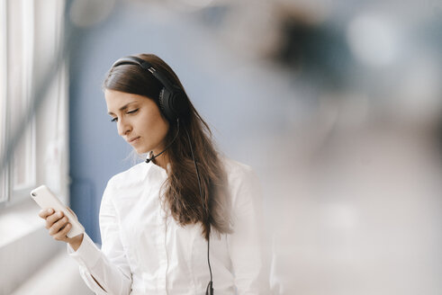 Junge Frau, die ein Smartphone benutzt und ein Headset trägt - KNSF03914