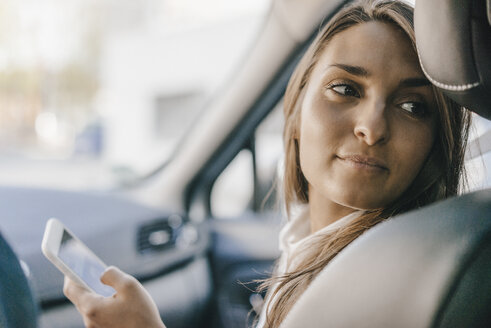 Junge Geschäftsfrau sitzt im Auto und benutzt ihr Smartphone - KNSF03920