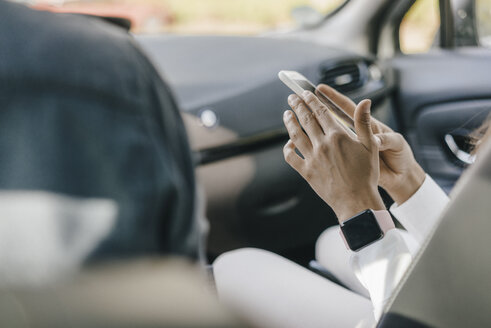 Junge Geschäftsfrau sitzt im Auto und benutzt ihr Smartphone - KNSF03921