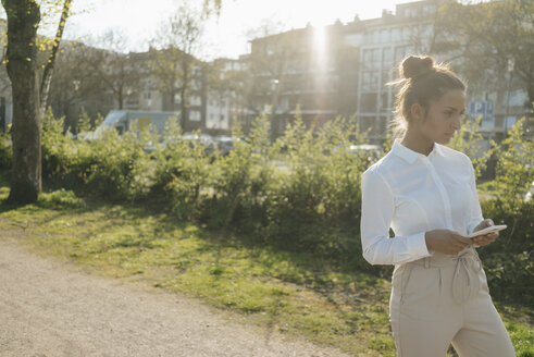 Junge Geschäftsfrau beim Spaziergang in der Stadt, mit einer Tasse Kaffee und einem Smartphone - KNSF03925