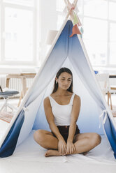 Junge Frau sitzt im Schneidersitz in einem Zelt zu Hause, mit geschlossenen Augen - KNSF03943
