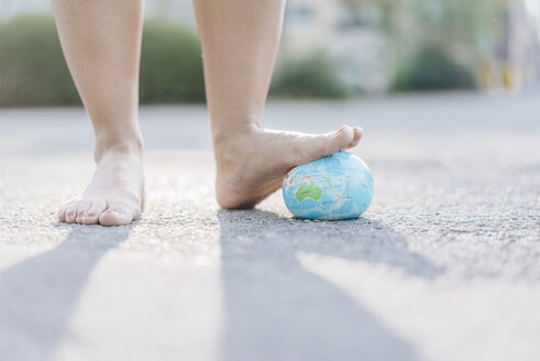Fuß einer jungen Frau, die auf eine Weltkugel tritt - KNSF03972