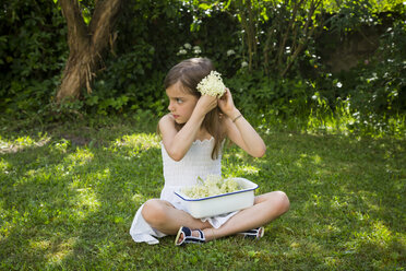 Kleines Mädchen sitzt auf einer Wiese im Garten mit einer Schale gepflückter Holunderblüten - LVF07021