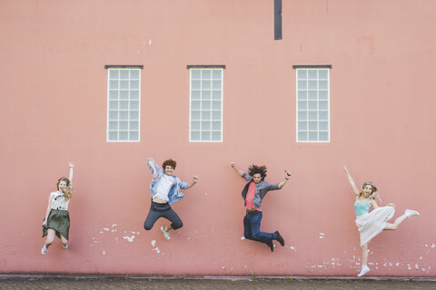 Freunde springen gegen rosa Wand Hintergrund, lizenzfreies Stockfoto