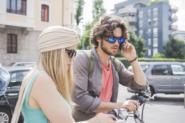 Couple using phone and walking along with push bikes - CUF22826