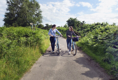 Zwei junge Erwachsene, die Fahrräder auf einem Feldweg schieben - CUF22842