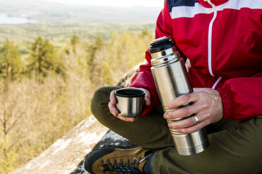 Cropped shot of male hiker sitting on mountain rock with tea flask, Russia - CUF22858