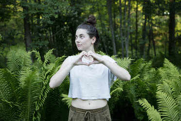 Young woman making heart shape hands in forest, Vogogna,Verbania, Piemonte, Italy - CUF22893