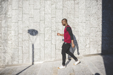 Young man walking outdoors, shadow cast on wall beside him - CUF22936