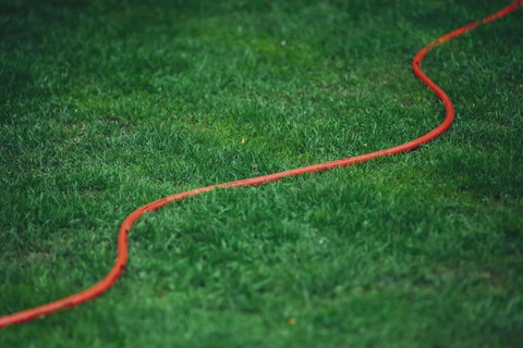Roter Gartenschlauch auf grünem Rasen, lizenzfreies Stockfoto