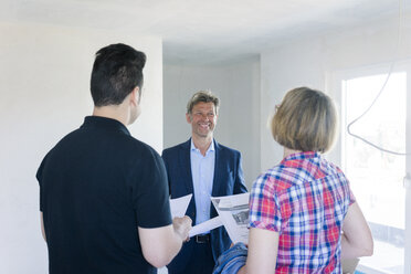 Smiling man in suit talking to couple in unfinished building - MOEF01229