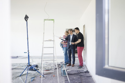 Mann im Anzug spricht mit Paar in unfertigem Gebäude, lizenzfreies Stockfoto