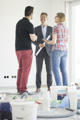 Smiling man in suit talking to couple in unfinished building - MOEF01240