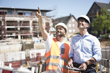 Lächelnder Bauarbeiter im Gespräch mit einem Mann auf der Baustelle - MOEF01259