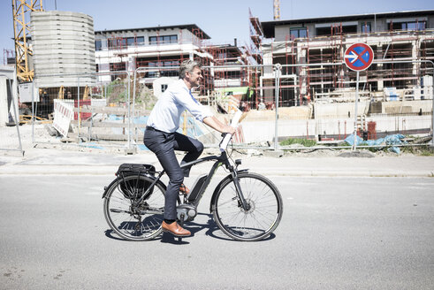 Lächelnder Mann auf E-Bike fährt entlang einer Baustelle - MOEF01262