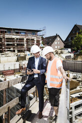 Mann im Anzug mit Tablet im Gespräch mit Bauarbeiter auf einer Baustelle - MOEF01265