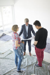 Man in suit and couple looking at blueprint in unfinished building - MOEF01271