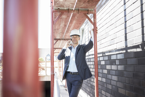 Architekt mit Mobiltelefon auf einem Baugerüst auf einer Baustelle, lizenzfreies Stockfoto
