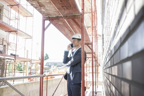 Architekt mit Mobiltelefon auf einem Baugerüst auf einer Baustelle, lizenzfreies Stockfoto