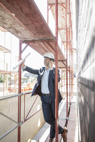 Architekt mit Mobiltelefon auf einem Baugerüst auf einer Baustelle, lizenzfreies Stockfoto