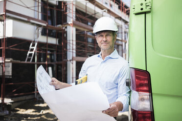 Portrait of architect with blueprint wearing hard hat on construction site - MOEF01298